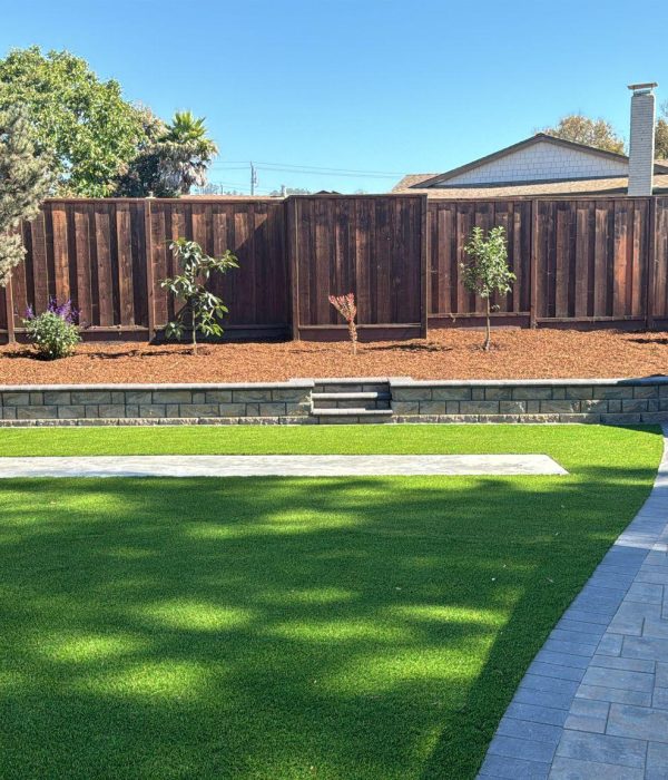 retaining wall a backyard with a fence and grass. Strong stone retaining wall lines the landscaping