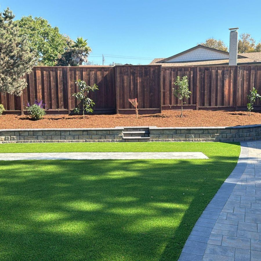 retaining wall a backyard with a fence and grass. Strong stone retaining wall lines the landscaping