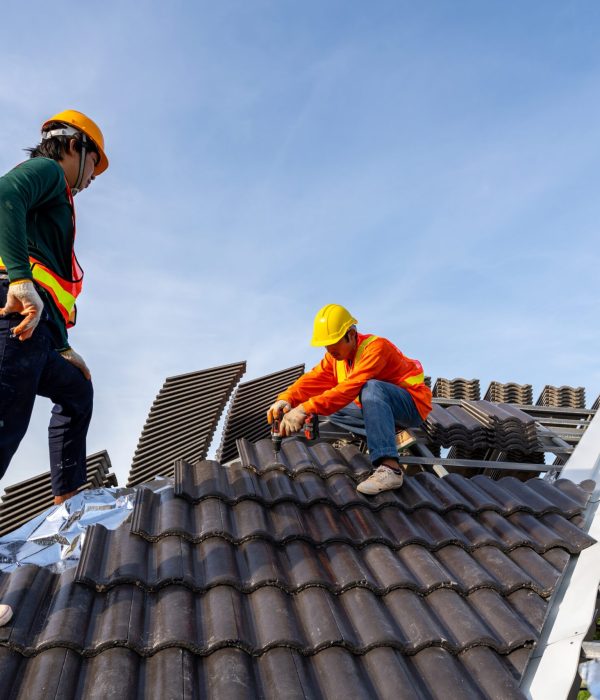 2 Construction workers install new roof at construction site, Electric drill used on new roofs with Concrete Roof Tiles. Concept of residential building under construction.