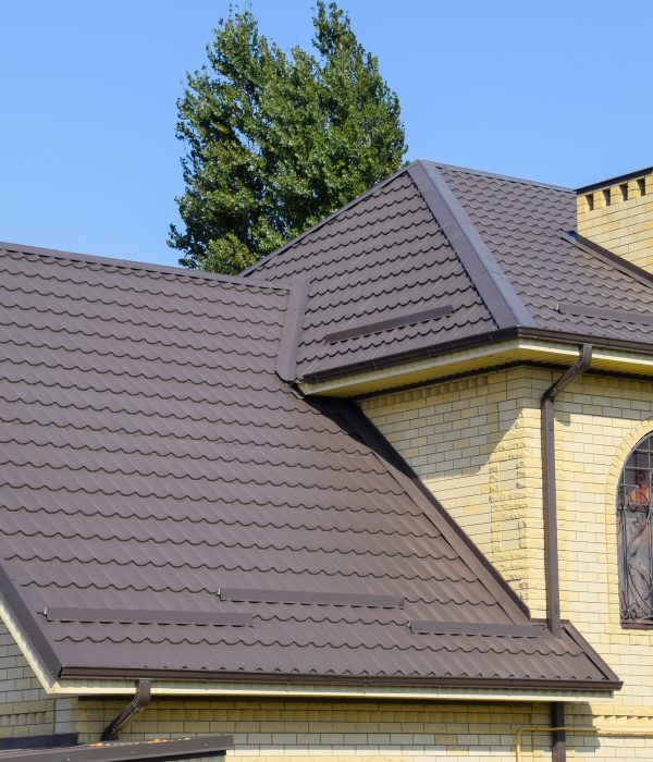 House of yellow brick and brown corrugated roof made of metal. Lattices on the windows
