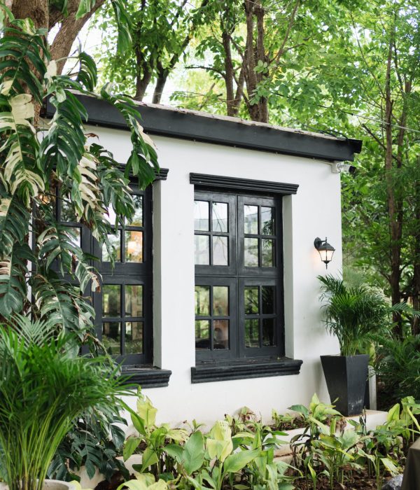 ADU Builder 47 Black frame window on white wall of house surrounded by lush tropical garden