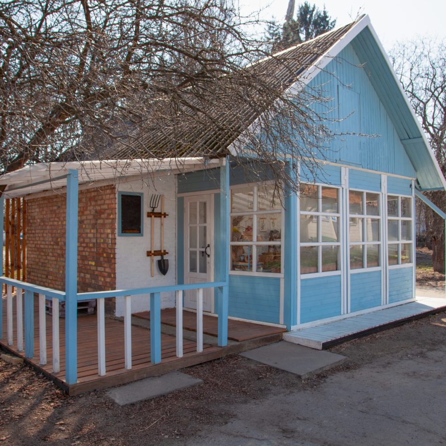 Country house cottage. Small wooden blue house in the garden. Shed. Garden tools – fork, shovel. Gardening. Cozy home. Spring time outdoor. Country house cottage. Small wooden house in the garden. Shed. Garden tools - fork, shovel. Gardening.