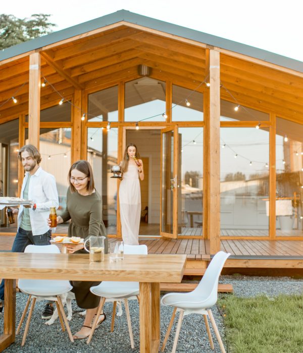 Happy friends carrying food preparing for the dinner on the backyard of the modern wooden house during the sunset