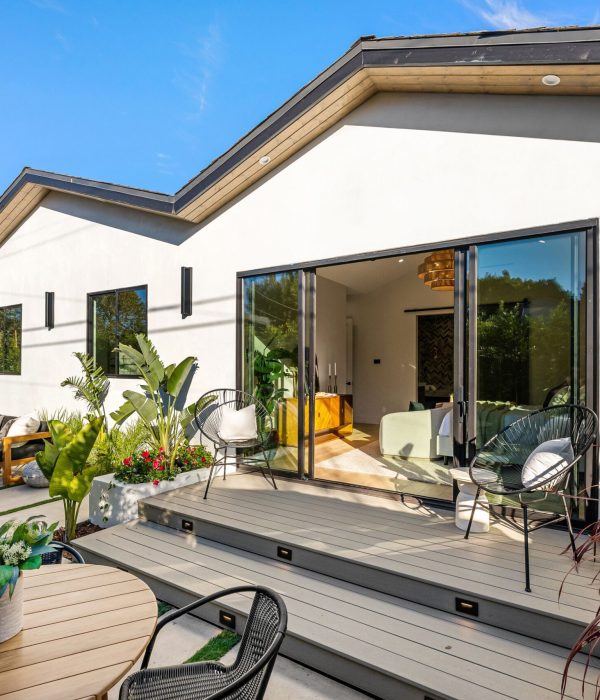 ADU Builder 52 Modern patio with outdoor furniture and plants, featuring a white house under a clear blue sky.